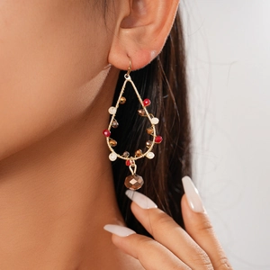 Détail de boucles d'oreilles en fil d'or avec des perles rouges, blanches et bronze