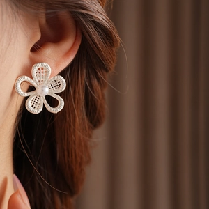 Gros plan d'une boucle d'oreille fleur en argent ajouré avec perle portée par un mannequin