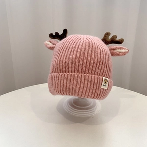 Close-up of pink knitted baby hat with reindeer antlers and ears on white stand