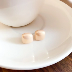 Macro shot of gold-plated square sugar cube pearl earrings on elegant white porcelain