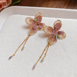 Dettaglio orecchini a fiore rosa intrecciato con catenine dorate e nappine