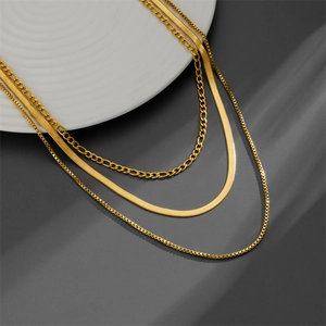 Three-piece layered gold necklace set featuring snake, figaro, and box chains on white plate