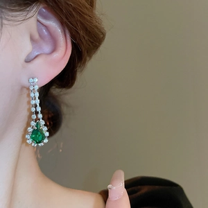 Close-up of a silver earring with sparkling diamonds and a green teardrop-shaped gemstone