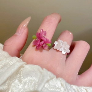 Close-up of handmade beaded flower rings in pink and white on a lace sleeve hand