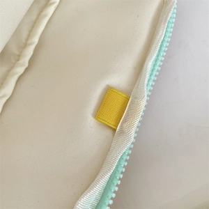 Detailed macro view of mint green zipper and yellow ribbon on off-white laptop sleeve