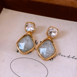 Macro shot of geometric gold earrings with clear crystals and grey fiber resin textures