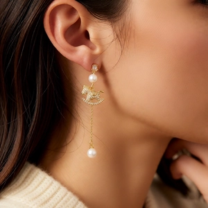 Detail of 18k gold plated earring featuring a rocking horse pendant and lustrous pearls