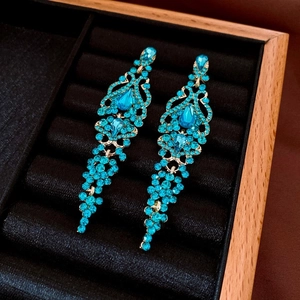 Detailed macro view of long blue rhinestone tassel earrings on a black velvet jewelry box