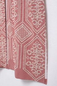 Detailed close-up of intricate white embroidery on a brick red bohemian style long coat