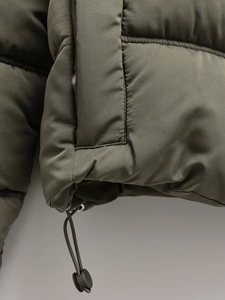Detail of army green quilted jacket fabric with adjustable hem drawstring and toggle