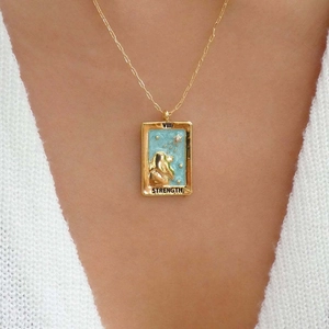 Close-up of gold tarot Strength pendant featuring turquoise enamel on a model