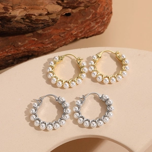 Close-up of gold and silver hoop earrings with white pearls on a minimalist stand