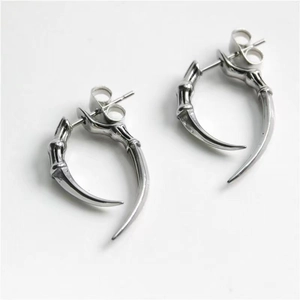 Macro shot of silver metal claw stud earrings with a sharp gothic fang design on white background