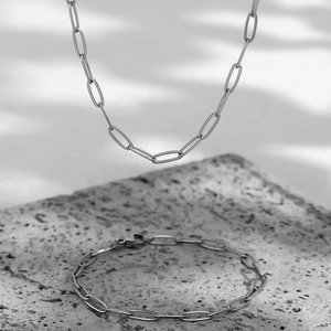 Detailed view of silver paperclip chain necklace and bracelet set on stone with water reflections