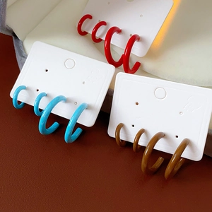Three pairs of C-shaped enamel earrings in red, blue, and brown on a professional display