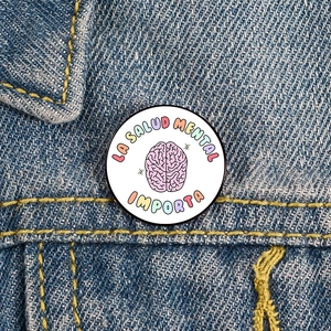 Detail of Mental Health Matters enamel pin on blue denim jacket with colorful Spanish text