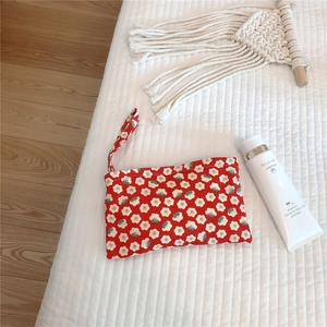 Macro detail of red floral cotton pouch with white daisy patterns on a white quilted mat