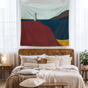 Artistic boho landscape tapestry with lighthouse design hanging over a wooden bed