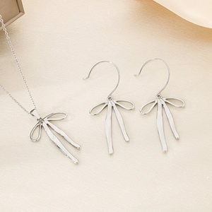 Detail of silver bow pendant necklace and earrings set on beige silk background