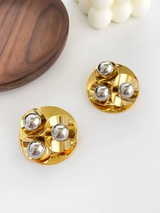 Detailed macro view of two-tone gold and silver geometric ball earrings on a wood tray
