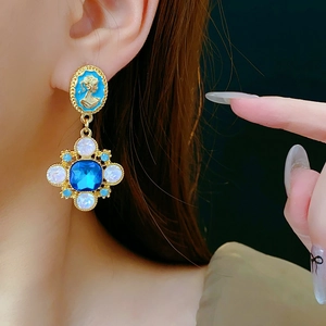 Close-up of vintage cameo earrings with blue stones and gold floral crystal details