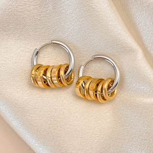 Detail of silver hoop earrings with five gold ring charms on luxury champagne silk fabric