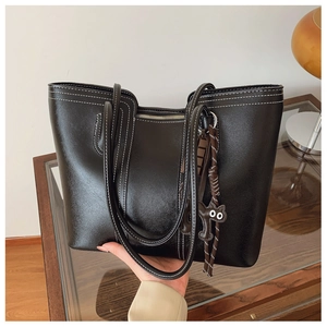 Detail of black leather tote bag featuring contrast white stitching and a cat charm