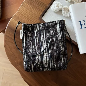 Detail of black and white striped woven crossbody bag on a wooden table with lace accents