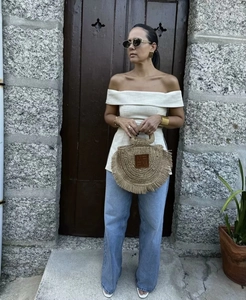Detail view of round straw bag with fringe and logo patch on casual chic outfit