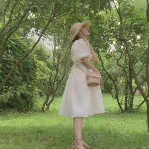 Detail of a handmade woven beige handbag with pearl chain styled on a cream puff sleeve dress