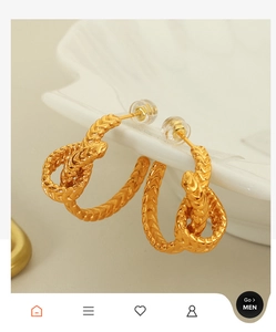 Gros plan de boucles d'oreilles nœud doré au design tressé sur un plateau coquillage