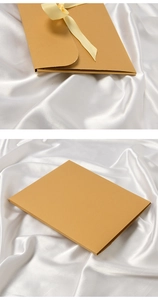 Detail of light brown envelope gift box with yellow ribbon on white silk background