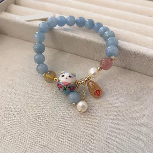 Blue beaded bracelet with maneki-neko lucky cat charm and pearls on linen display box