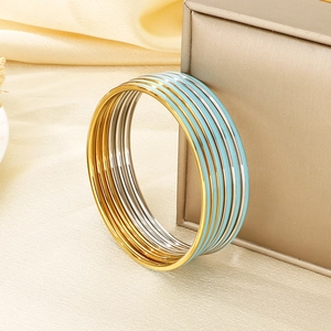 Detail of stacked gold, silver, and blue enamel bangle bracelets on a silk background