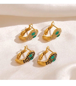 Détail de deux paires de créoles serpent dorées avec cristaux verts et clairs sur de la soie