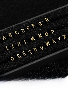 Macro view of golden S925 sterling silver alphabet A-Z piercing studs set in a luxury tray