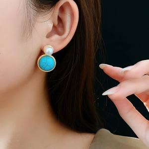 Detail of vintage-style gold earrings with a white pearl and round turquoise stone