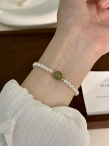 Close-up of pearl bracelet with green jade bead and golden spacers on a wrist