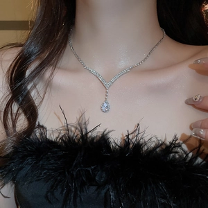 Close-up of silver V-shaped necklace with teardrop zircon worn by a model in black