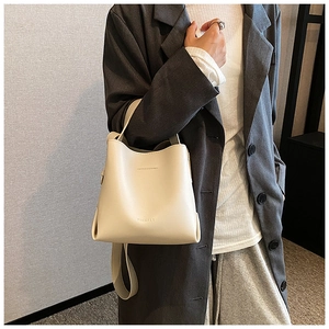 Detailed shot of a beige matte leather bucket bag worn by a model in a minimal outfit