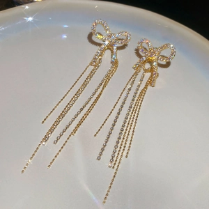 Close-up of golden bow earrings with zircon tassels on an elegant ceramic plate