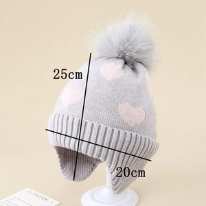 Detail of grey winter knit hat with pink hearts, earflaps and large fluffy pompom