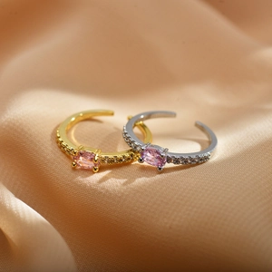 Macro view of adjustable copper rings with pink oval zircons on champagne satin background