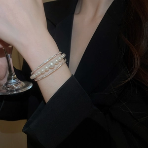 Detail of layered pearl and rhinestone cuff bracelet worn by a model holding a glass