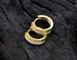 Detailed macro view of gold hoop earrings set with colorful rectangular zircons on wood