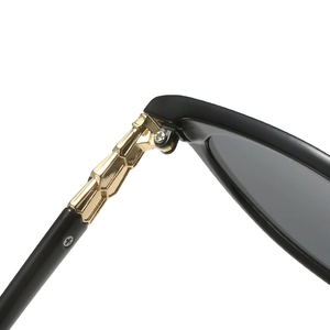 Side view of black sunglasses featuring a segmented gold metal hinge and grey lenses