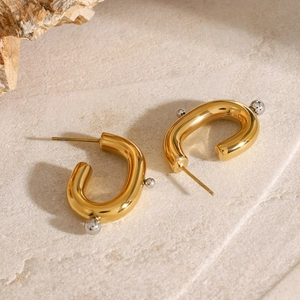 Detail of gold U-shaped earrings with inlaid silver beads on textured stone surface