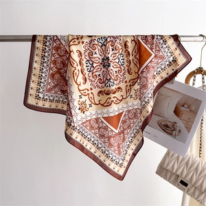 Brown and beige paisley silk scarf draped on a metal rack with lifestyle props