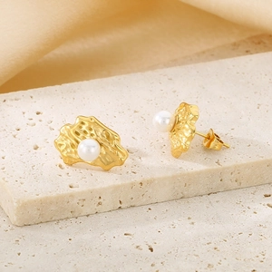 Detailed view of gold irregular textured pearl stud earrings on a stone display