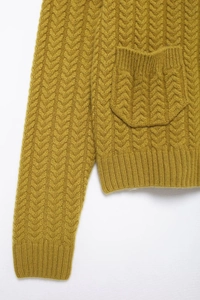 Detail of a ginger yellow cable knit cardigan showing the textured pocket and ribbed cuff